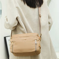 Cream waterproof nylon crossbody bag worn with adjustable strap