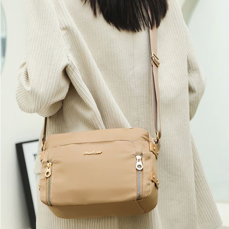 Cream waterproof nylon crossbody bag worn with adjustable strap