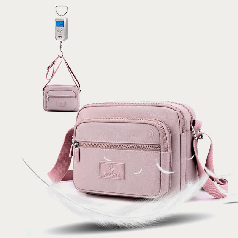 Light pink four-zip crossbody bag hanging from its adjustable strap