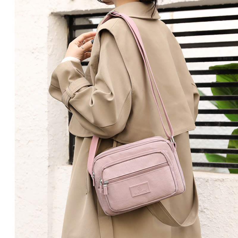 Light pink four-zip nylon crossbody bag worn at the hip