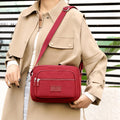 Brick red four-zip nylon crossbody bag worn at the front