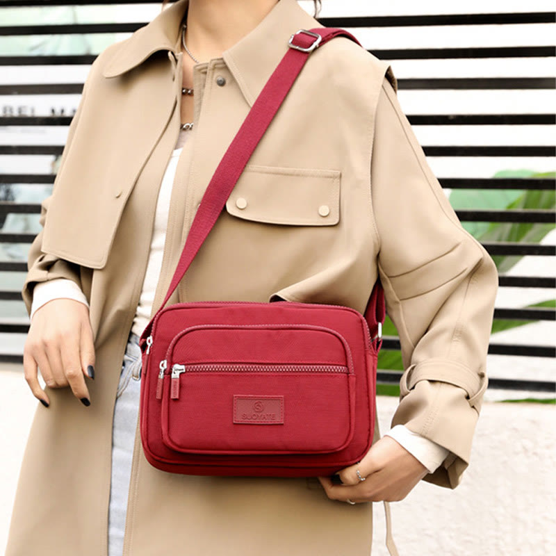 Brick red four-zip nylon crossbody bag worn at the front